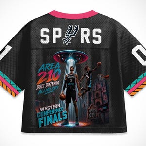 Op de afbeelding: Zwart mesh basketbalshirt met het woord "SPURS" in witte blokletters. Het shirt heeft een afbeelding van twee basketballers onder een UFO, met de tekst "AREA 210" en "WESTERN CONFERENCE FINALS". Het shirt heeft een roze kraag en kleurrijke afwerking.