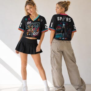 Op de afbeelding: Twee mensen dragen zwart-witte sportshirts met de tekst "GO SPURS GO!" en "SPURS" op de rug. De shirts hebben kleurrijke randen en afbeeldingen. E&eacute;n persoon draagt een zwarte geplooide rok, de ander een beige cargobroek.