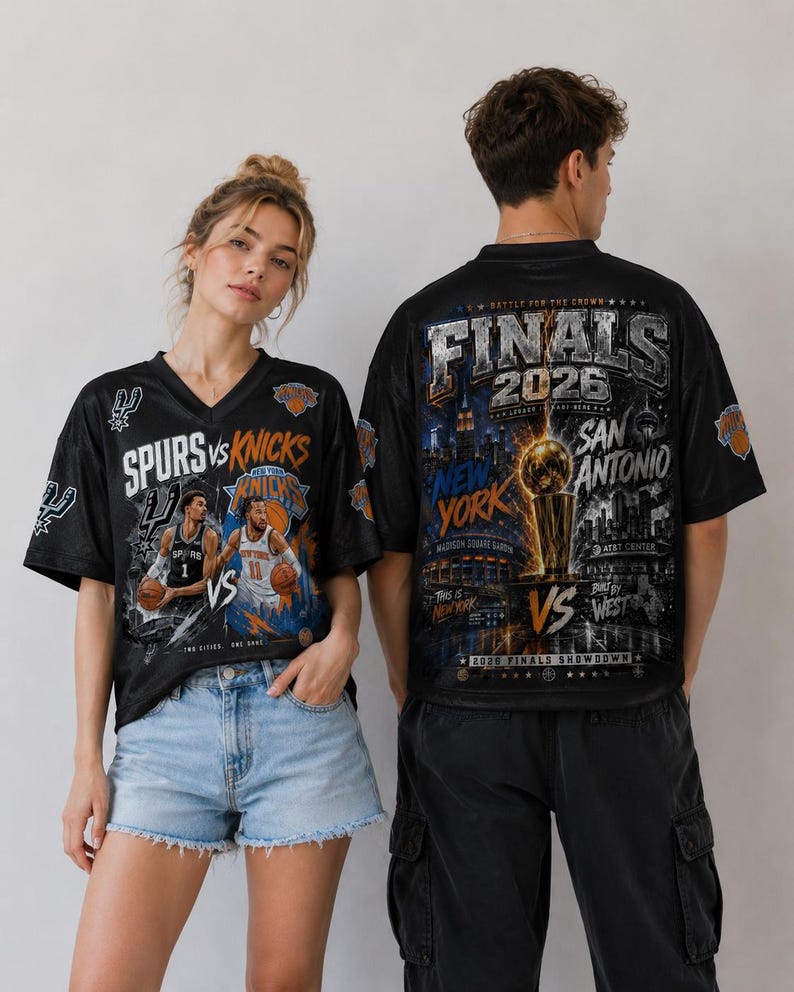K&ouml;nnte beinhalten: Ein schwarzes T-Shirt mit V-Ausschnitt, das auf der Vorderseite eine Grafik des Basketball-Spiels Spurs gegen Knicks und auf der R&uuml;ckseite eine gro&szlig;e Grafik der Finals 2026 zeigt, inklusive Larry O'Brien Troph&auml;e, Skylines und Teamlogos.