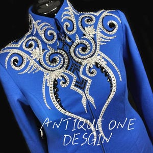 Könnte beinhalten: Königsblaue Reitjacke mit aufwendigen Verzierungen aus silbernen, schwarzen und klaren Kristallen. Die Jacke hat einen hohen Kragen und einen durchgehenden Reißverschluss. Der Text "ANTIQUE ONE DESIGN" ist unten sichtbar.