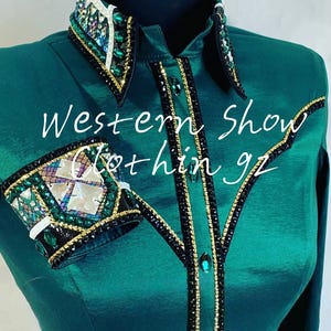 May include: Emerald green Western show shirt with ornate embellishments. The collar and cuffs feature a mix of iridescent, emerald, and clear crystals, with gold and black accents. The shirt has a button-down front and the text "Western Show Clothing gz".