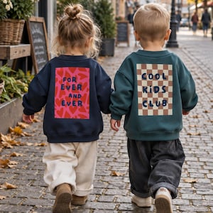Könnte beinhalten: Zwei langärmelige Sweatshirts, eines in Marineblau mit rosa Herzmuster und dem Text "FOR EVER AND EVER" und eines in Dunkelgrün mit braun-weißem Karomuster und dem Text "COOL KIDS CLUB", jeweils auf die Rückseite der Kleidungsstücke gedruckt.