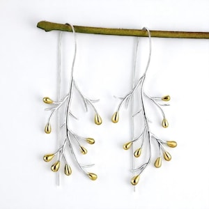 May include: Silver-tone branch earrings with gold-colored teardrop accents. The earrings hang from a thin silver wire and are displayed against a white background. The earrings are a nature-inspired jewelry design.