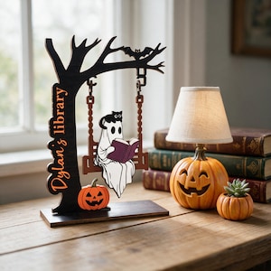 May include: A black wooden tree-shaped display stand with the text Dylan's library, featuring a hanging swing with a white ghost reading a purple book and a black cat on its head, plus a small orange jack-o'-lantern at the base of the tree.
