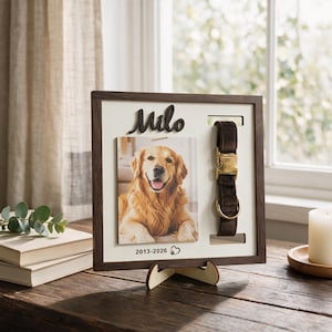 May include: A square wooden memorial frame featuring a dark brown border and a white backing. The frame displays a photograph of a golden retriever, the name Milo in black script, and the dates 2013-2026 with a heart and paw print icon.