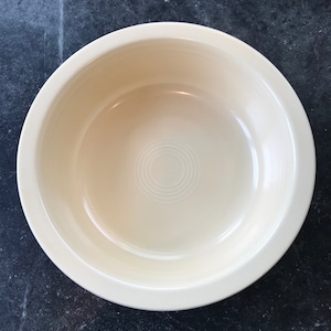 May include: A white ceramic bowl with a smooth, glossy finish. The bowl has a slightly raised rim and a circular design in the center.