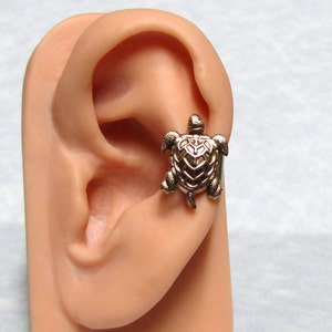 May include: A gold-toned turtle ear cuff. The turtle is detailed with a textured shell and is positioned on the upper part of the ear.