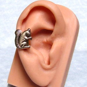 May include: A gold-toned squirrel ear cuff. The squirrel is perched on the edge of the ear, facing forward. The ear cuff is designed to fit on the upper part of the ear.