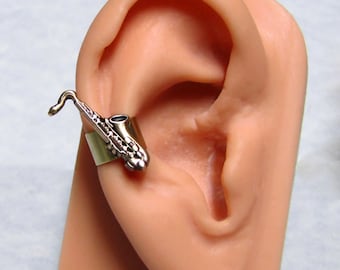 May include: A gold-toned saxophone ear cuff. The saxophone is detailed with a black mouthpiece and a silver band. The ear cuff is designed to fit on the upper part of the ear.