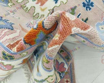 May include: A rolled-up area rug with a floral pattern in shades of pink, orange, blue, and white. The rug has a fringed edge and a detailed design, showcasing a blend of colors and textures.