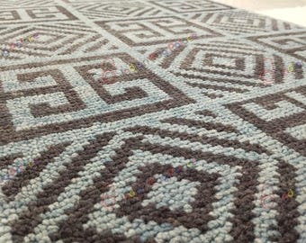 May include: Close-up of a blue and grey patterned rug. The rug features a repeating geometric design with dark grey shapes on a light blue background. The texture appears soft and plush.