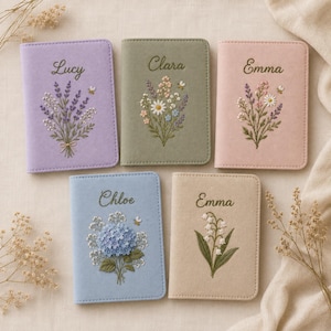 Könnte beinhalten: Fünf rechteckige Reisepasshüllen in Lavendel, Salbeigrün, Blassrosa, Hellblau und Beige. Jede ist mit gestickten Blumensträußen, einer kleinen Biene und einem Namen versehen: Lucy, Clara, Emma, Chloe und Emma, gestickt in dunkelbraunem Garn.
