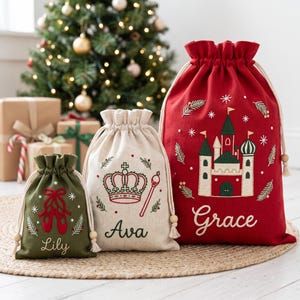 May include: Three drawstring gift bags in red, cream, and olive green. The olive bag features red ballet slippers and the name Lily. The cream bag shows a crown, a scepter, and the name Ava. The red bag displays a castle and the name Grace.