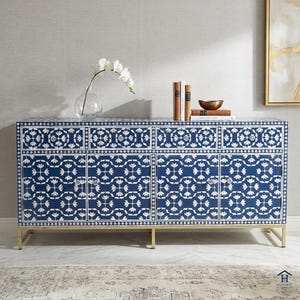 Könnte beinhalten: Ein marineblaues und weiß gemustertes Sideboard mit goldenen Beinen. Der Schrank hat vier Türen und drei Schubladen. Eine Glasvase mit weißen Blumen, Bücher und eine Schale stehen oben auf dem Schrank.