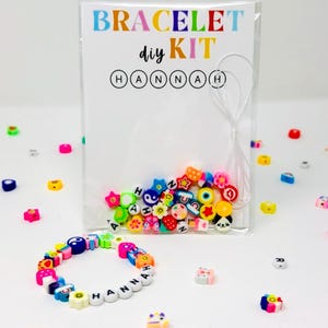 May include: A DIY bracelet kit with colorful beads and the name "HANNAH" spelled out. The kit includes a variety of beads in different shapes and colors, including stars, flowers, and letters. The kit is packaged in a clear plastic bag with the words "BRACELET diy KIT".