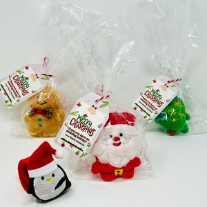 May include: Christmas-themed gift bags featuring plush figures of a penguin, Santa Claus, a gingerbread man, and a Christmas tree. Each bag includes a tag with the text "Merry Christmas" and a holiday message.
