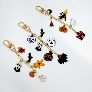 May include: Three gold-colored keychains with Halloween-themed charms. Each keychain features a variety of charms, including ghosts, bats, pumpkins, and haunted houses. The charms are in black, orange, white, and gold.