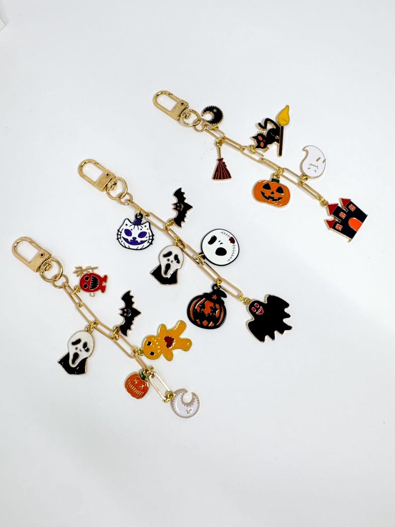 May include: Three gold-colored keychains with Halloween-themed charms. Each keychain features a variety of charms, including ghosts, bats, pumpkins, and haunted houses. The charms are in black, orange, white, and gold.