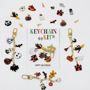 May include: A Halloween-themed keychain DIY kit with various charms, including pumpkins, ghosts, bats, and witch hats. The kit includes gold-colored keychains and a card that reads "KEYCHAIN DIY KIT" and "HAPPY HALLOWEEN!"
