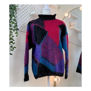 Peut inclure: Un pull vintage en patchwork avec un col roulé haut. Le pull présente un motif de blocs de couleurs avec des sections noires, violettes, roses et bleues. Les coutures sont accentuées de coutures contrastantes, créant un look texturé unique.