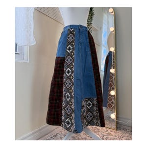 Peut inclure: Longue jupe en jean avec des panneaux patchwork. La jupe présente des panneaux en jean bleu, en tartan marron et en tissu à motifs. La jupe est présentée sur un mannequin. La jupe a une taille haute et une longue silhouette fluide.