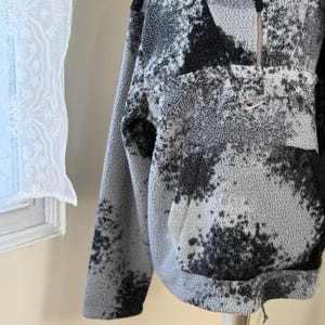 K&ouml;nnte beinhalten: Grau-schwarzer Fleece-Pullover mit Viertelrei&szlig;verschluss und K&auml;ngurutasche. Der Pullover hat ein gesprenkeltes Muster und ein kleines Nike-Logo auf der Brust. Der Kordelzug am Saum erm&ouml;glicht eine individuelle Passform.