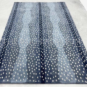 May include: A rectangular area rug with a striped pattern in shades of blue and white. The rug features vertical stripes of varying shades of blue, with a speckled pattern of white dots throughout. The text "THE RUG PALACE IN" is visible.