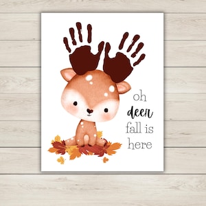 Puede incluir: Una impresi&oacute;n caprichosa con un ciervo de dibujos animados con astas de huellas de manos, sentado sobre hojas de oto&ntilde;o. El texto "oh deer fall is here" est&aacute; en negro. Fondo blanco.