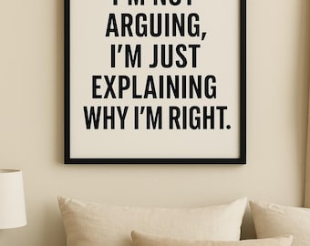 May include: Black framed wall art with the text "I'M NOT ARGUING, I'M JUST EXPLAINING WHY I'M RIGHT." The artwork is displayed above a bed with beige bedding and pillows. A small black side table with a lamp is visible.