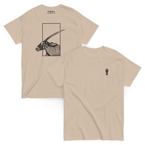 Peut inclure: Deux t-shirts beiges. L'un présente une illustration en noir et blanc d'un oryx dans un rectangle, avec "NAMIBIA ROADSIDE" au-dessus. L'autre a un petit graphisme noir sur la poitrine. Les deux sont à manches courtes.