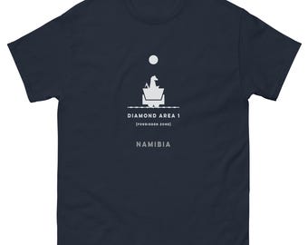 May include: Navy blue t-shirt with a white graphic design featuring a geometric shape, a circle, and the text "DIAMOND AREA 1 [FORBIDDEN ZONE] NAMIBIA". The shirt is made of a soft, comfortable material.