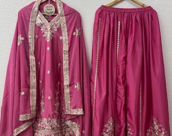 Op de afbeelding: Een magenta tweedelige outfit met ingewikkelde gouden borduursels en versieringen. De set bevat een top met lange mouwen en een V-hals en een zwierige rok. De outfit wordt gepresenteerd op houten hangers.