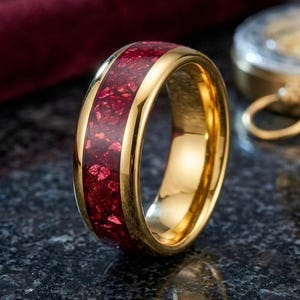以下が含まれることがあります： 深紅色のテクスチャード加工された素材のバンドが付いた、金色のリング。 リングは研磨された反射面を持っています。 背景には暗い表面とコンパスのちらつきが含まれています。