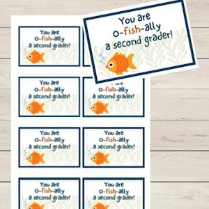 May include: Printable cards with the text "You are o-fish-ally a second grader!" and a cartoon goldfish. The cards are in a rectangular shape with a blue border and a white background. The words "Good Things Printables" are at the top.