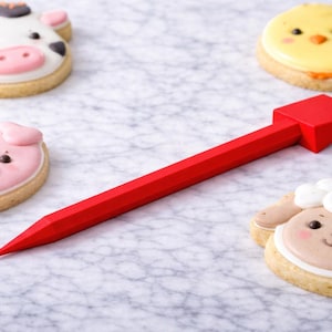 Peut inclure: Une flèche rouge pointe vers quatre biscuits au sucre décorés. Les biscuits ont la forme d'une vache, d'un cochon, d'un poussin et d'un mouton. Les biscuits ont un glaçage détaillé et sont sur une surface claire.