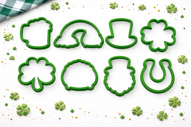 Peut inclure: Huit emporte-pi&egrave;ces en plastique vert repr&eacute;sentant des symboles de la Saint-Patrick, comme une chope de bi&egrave;re, un arc-en-ciel, un chapeau haut de forme, un tr&egrave;fle et un fer &agrave; cheval. Ils sont dispos&eacute;s sur une surface blanche avec des confettis.