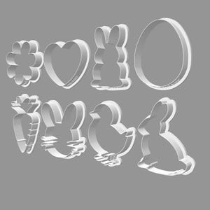 May include: A collection of eight white metal cookie cutters in various Easter-themed shapes. The shapes include a flower, heart, bunny, egg, carrot, bunny head, chick, and a bunny.
