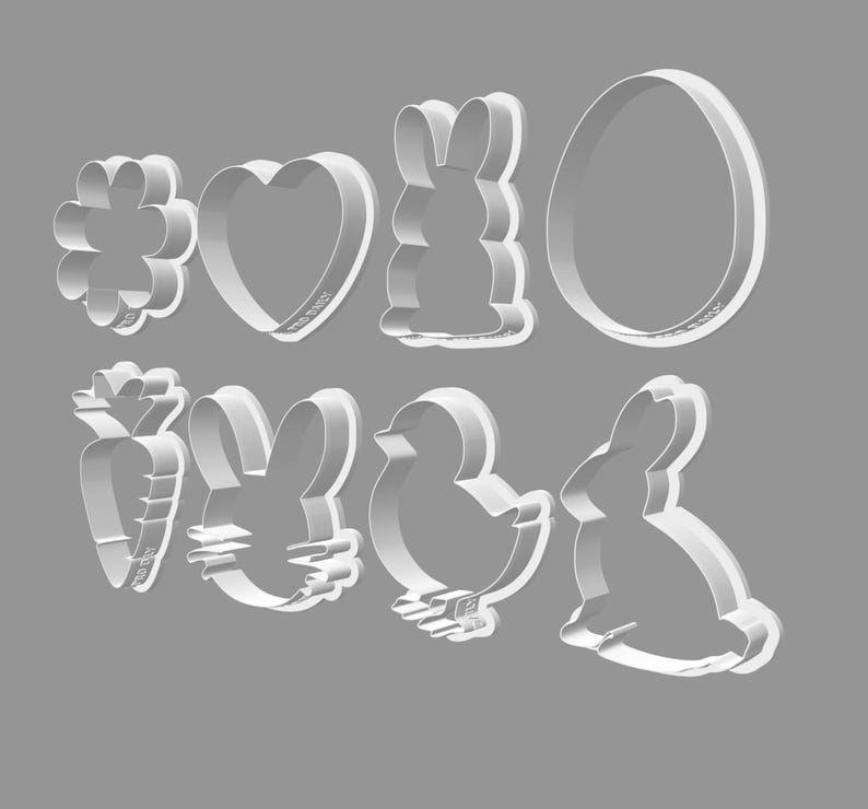 May include: A collection of eight white metal cookie cutters in various Easter-themed shapes. The shapes include a flower, heart, bunny, egg, carrot, bunny head, chick, and a bunny.