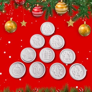 May include: A collection of white Christmas-themed wax seals with various embossed designs, including a Christmas tree, snowman, and angel, arranged on a red background with festive ornaments and greenery.