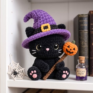 May include: A black crocheted cat plush toy wearing a purple witch hat with a yellow buckle. The cat has large black eyes, a pink nose, and pink paw pads. It holds a brown stick topped with a small orange crocheted pumpkin jack-o'-lantern.