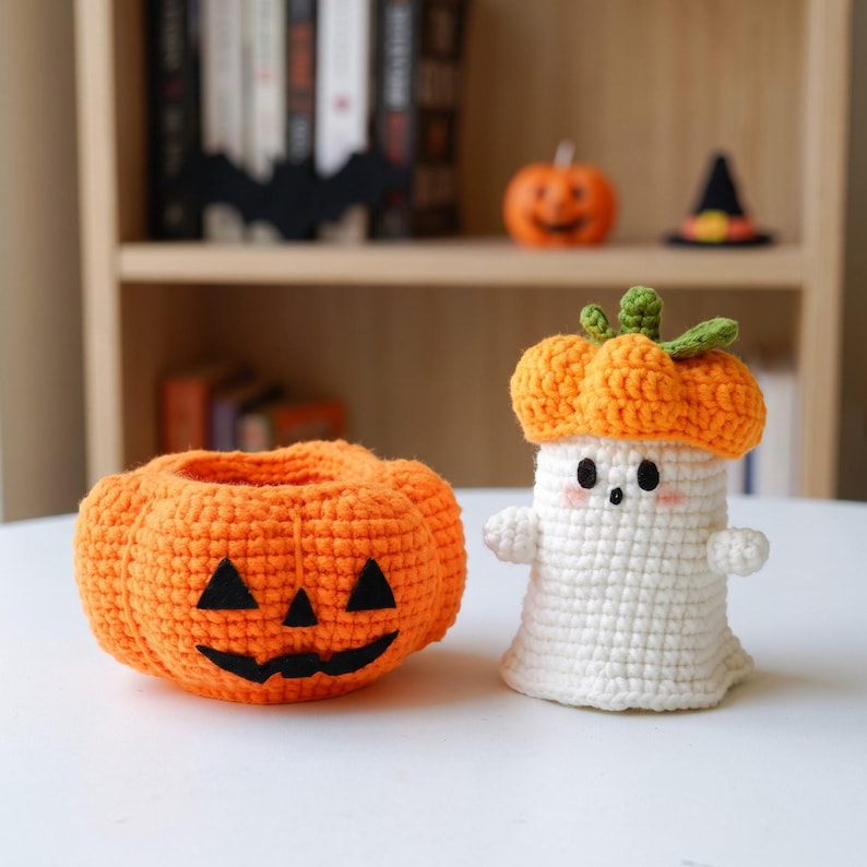May include: A crochet jack-o'-lantern bowl with a black felt face and a white crochet ghost figure wearing an orange pumpkin hat. The ghost has small black eyes, a tiny mouth, and pink blush on its cheeks, with a green stem on its hat.