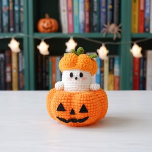 May include: A handmade crochet amigurumi featuring a small white ghost with black eyes and pink cheeks, wearing an orange pumpkin hat, sitting inside a larger orange crochet pumpkin with a black felt jack-o'-lantern face and green stem.