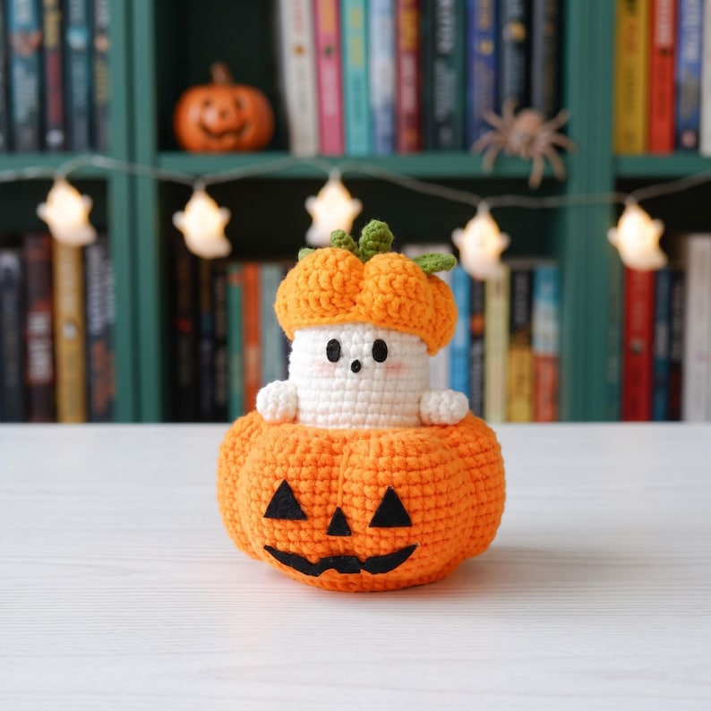 May include: A handmade crochet amigurumi featuring a small white ghost with black eyes and pink cheeks, wearing an orange pumpkin hat, sitting inside a larger orange crochet pumpkin with a black felt jack-o'-lantern face and green stem.