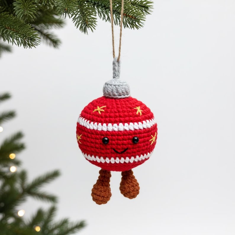 Peut inclure: Ornement de No&euml;l en crochet rouge, orn&eacute; de rayures blanches et d'&eacute;toiles jaunes. Il pr&eacute;sente un visage souriant, un dessus gris et des jambes marron. Suspendu &agrave; une ficelle naturelle, id&eacute;al pour les f&ecirc;tes.
