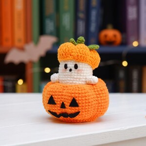 May include: A crocheted amigurumi figure featuring a small white ghost with a round face and black eyes, wearing an orange pumpkin hat. The ghost sits inside a larger, round orange crocheted pumpkin with a black felt jack-o'-lantern face.