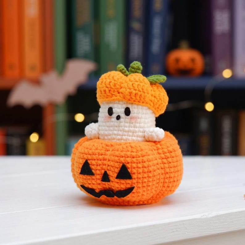 May include: A crocheted amigurumi figure featuring a small white ghost with a round face and black eyes, wearing an orange pumpkin hat. The ghost sits inside a larger, round orange crocheted pumpkin with a black felt jack-o'-lantern face.
