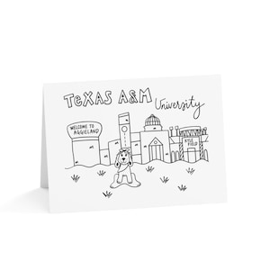 May include: A white greeting card featuring a black line drawing of the Texas A&M University campus. The illustration includes a dog in the foreground, a sign reading Welcome to Aggieland, and a stadium labeled Kyle Field in the background.