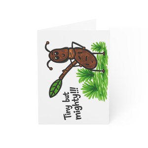 May include: A white greeting card featuring a cartoon ant holding a leaf. The ant is brown with black details and the text "Tiny but mighty!!!" is written in black. Green foliage is drawn in the background.
