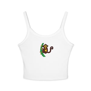 May include: White vest top featuring a cartoon monkey design. The monkey is brown with a yellow face and hangs from a green vine. The top has thin straps and a scoop neckline.