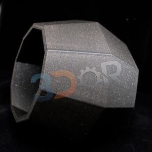 May include: A dark grey, geometric object with a textured surface. The item has a multi-faceted design and appears to be made of a solid material. The object is set against a black background, highlighting its form.
